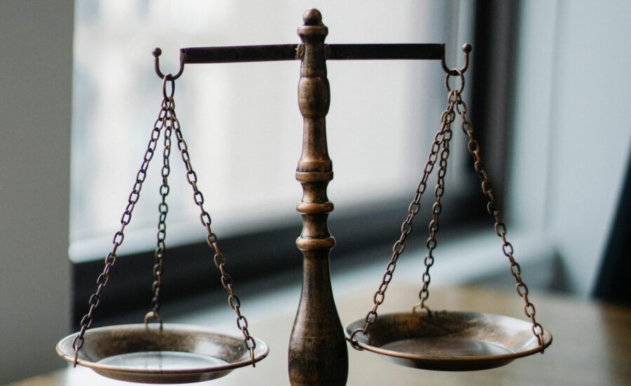 Decorative judgement scale and gavel placed on desk in light lawyer office against window